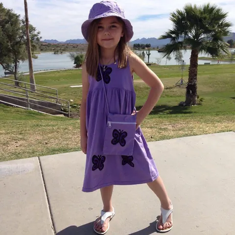 Girl in a lavender butterfly sundress with a matching purse and hat