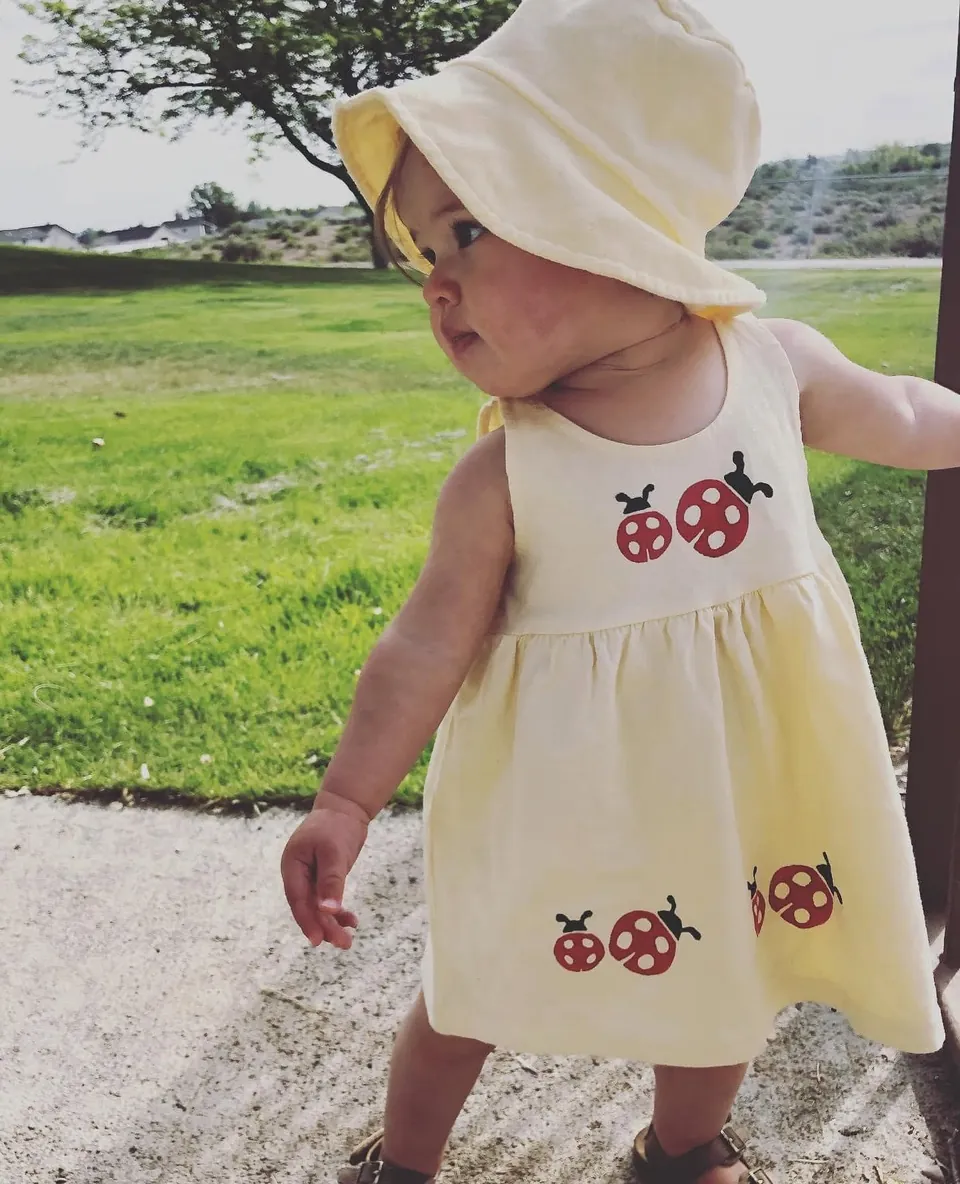 Toddler in a cream sundress and bucket hat stamped with red ladybugs