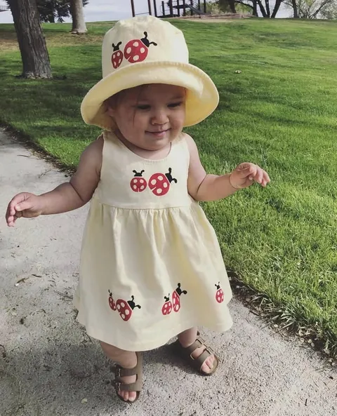 Toddler in a cream ladybug sundress and matching sun hat