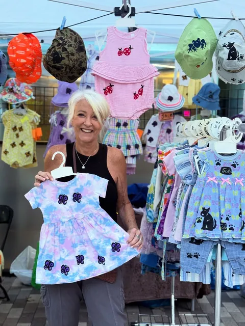 The maker holding up a tie-dye butterfly dress at the Inky Binky Bonky booth