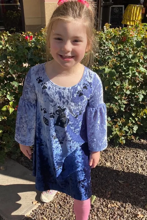 Girl in a blue crushed-velvet dress stamped with a puppy and paw prints